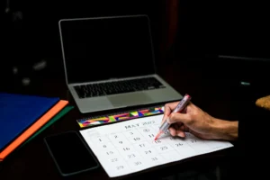 A person plans on a calendar at a desk with a laptop and phone, May 2022.